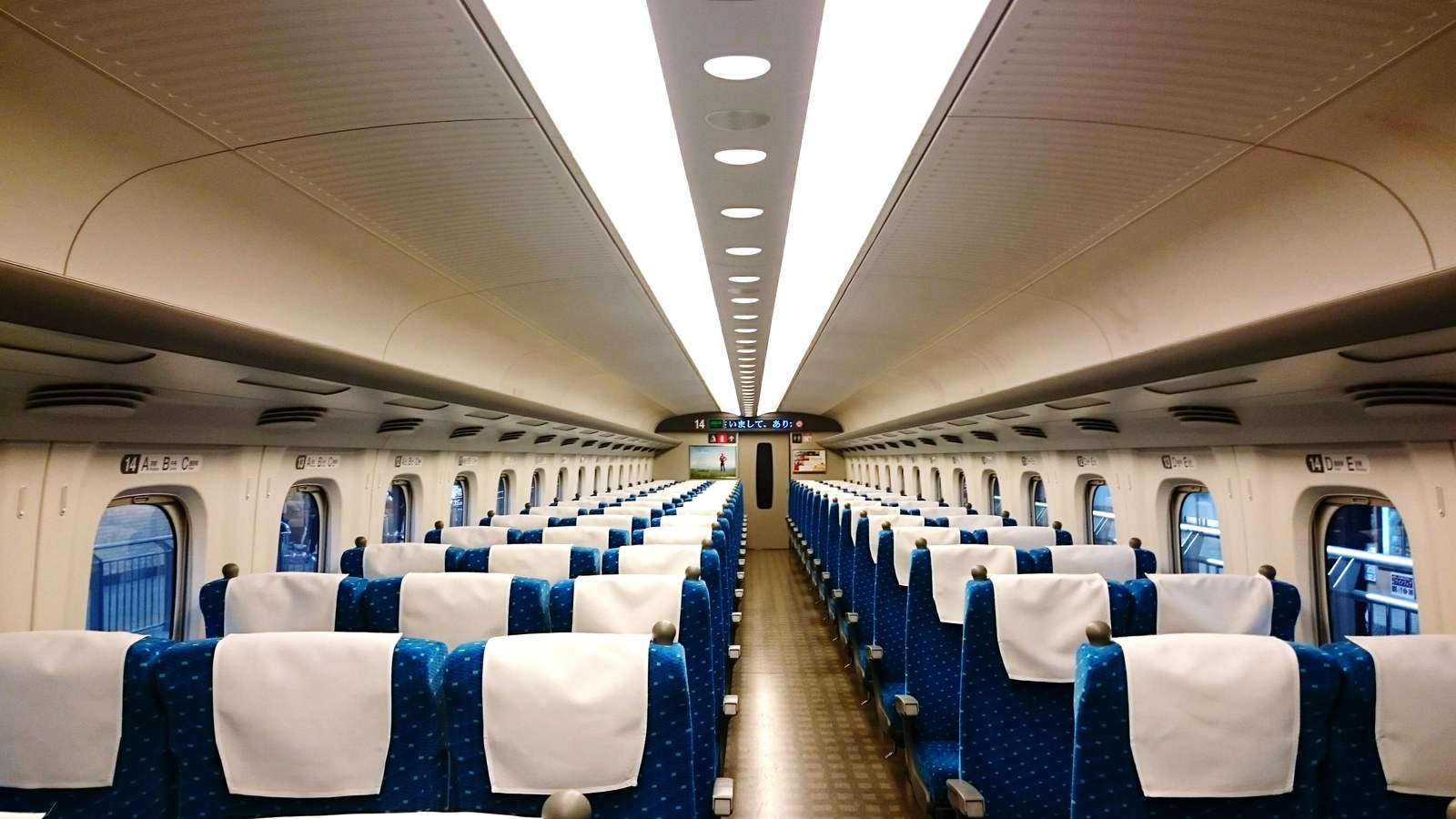 Interior espaçoso e silencioso de vagão do Shinkansen japonês com fileiras de poltronas reclináveis bandejas individuais e piso limpo - NANI JLPT